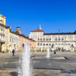 grande piazza di Torino con getti d'acqua dal pavimento circondata da palazzi storici reali